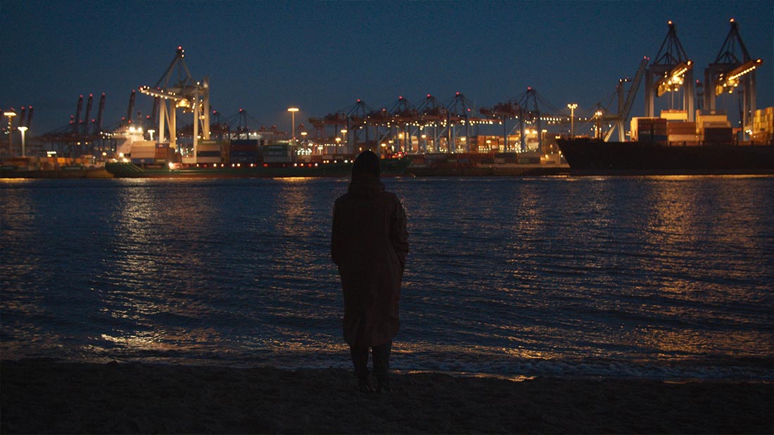 Eine Frau schaut in der blauen Stunde auf die Hafen-Lichter .