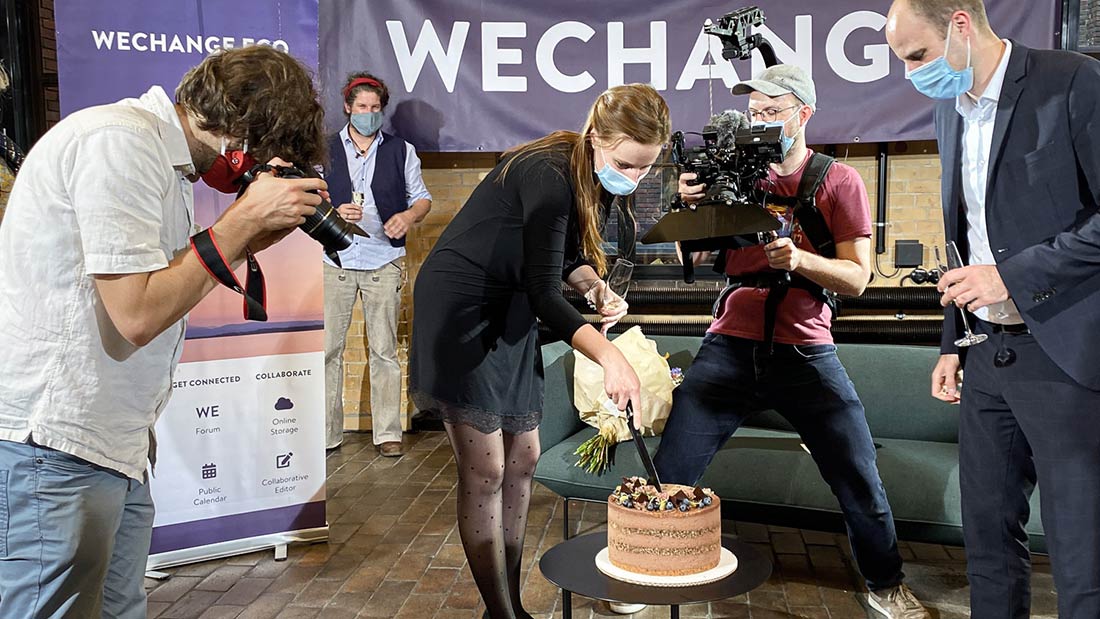 Behind-the-scenes Foto vom Dreh der Social Media Portraits für Dialogue for Future. Eine Torte wird angeschnitten. Daneben stehen Menschen mit Sektgläsern. Ein Fotograf und ein Kameramann halten die Szene fest.