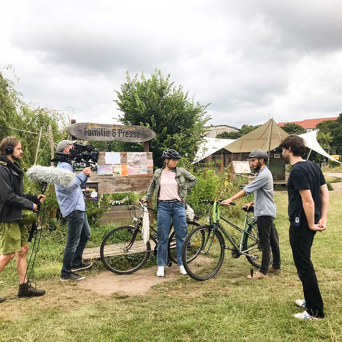 Making-Of-Foto Erklärfilm Suffizienzdetektive für Deutsche Umweltstiftung. Zwei junge Menschen mit Fahrrädern stehen vor einer Infotafel an einem Garten-Projekt.